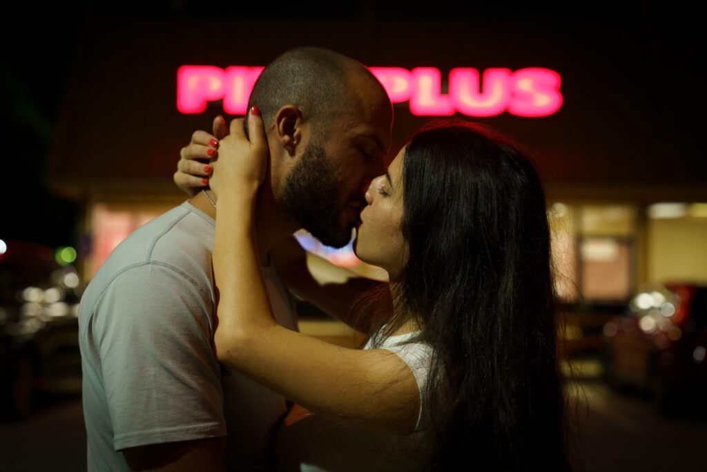 Close portrait of a couple kissing with a neon sign glowing pink behind them