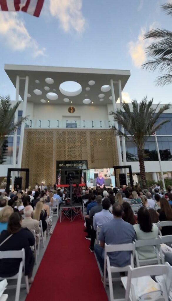 Red carpet aisle and seated crowd facing a modern building marked Golden Beach at dusk