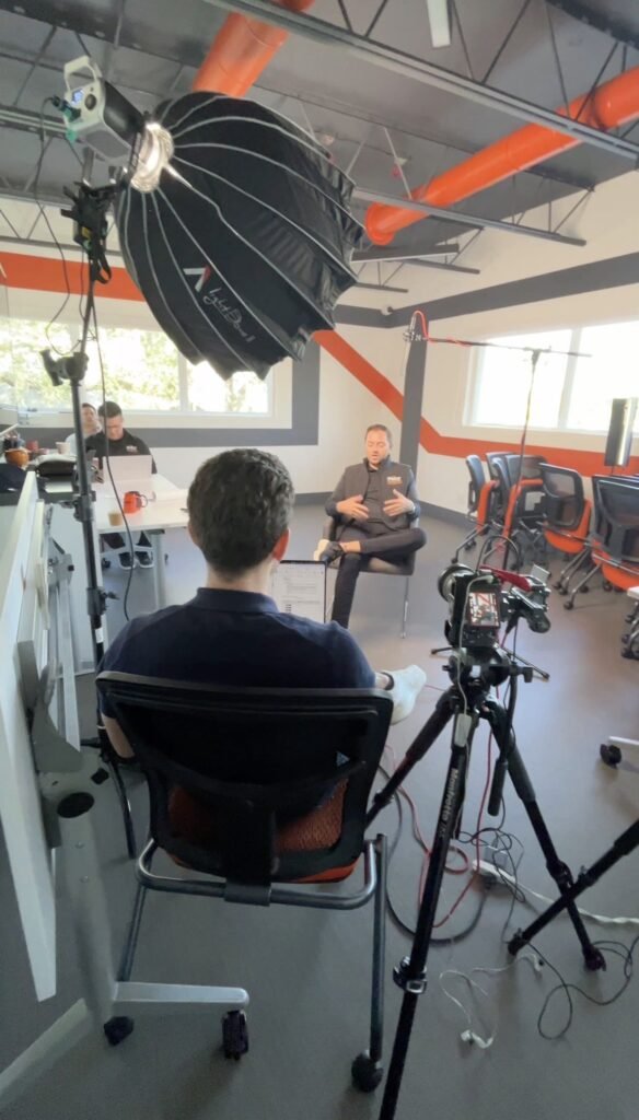 Interview lit with a large overhead softbox in an open-plan office, subject seated at the far end