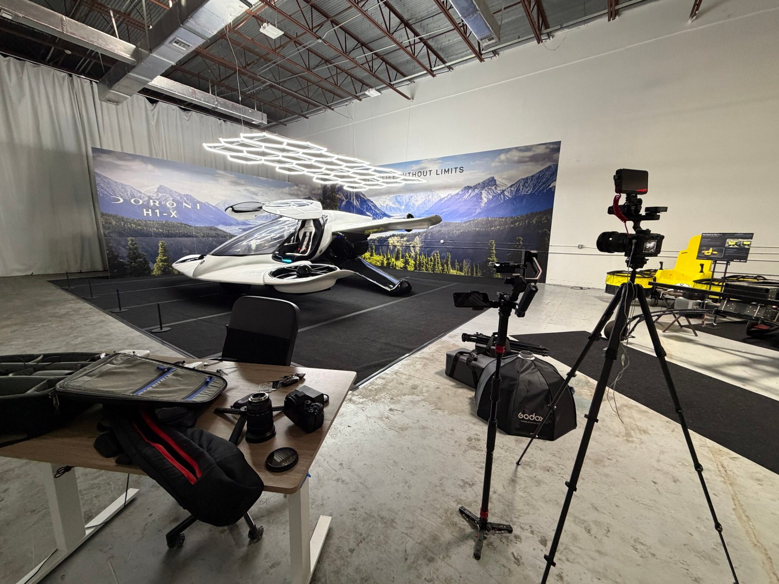 The full-scale Doroni H1-X on a black stage in front of a mountain backdrop reading Life Without Limits, with camera gear staged in the foreground