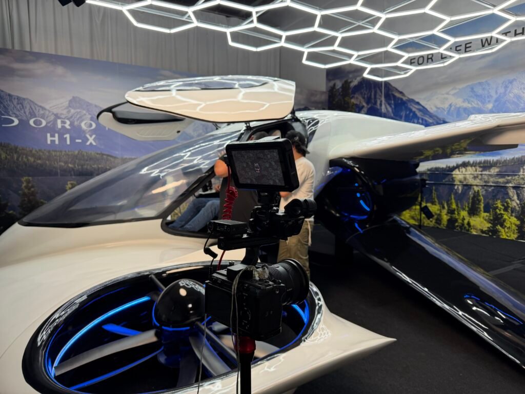 A camera rig with monitor set up at the nose of the Doroni H1-X, its ducted rotor lit blue beneath the hexagonal ceiling lights