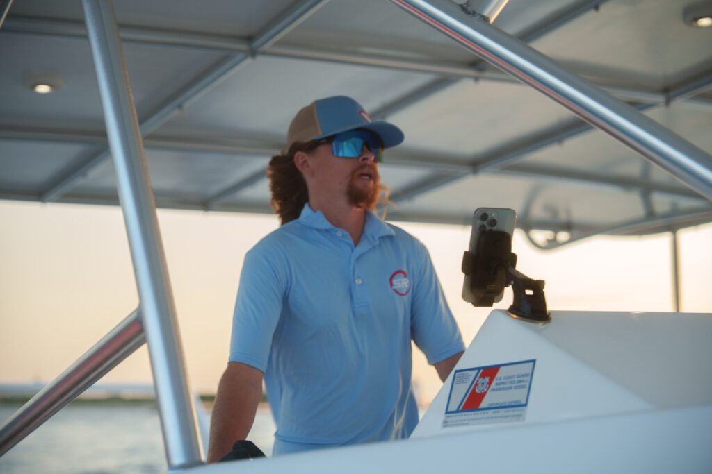 Sea Rocket crew member at the helm in a company polo holding the radio handset as the boat runs at sunset