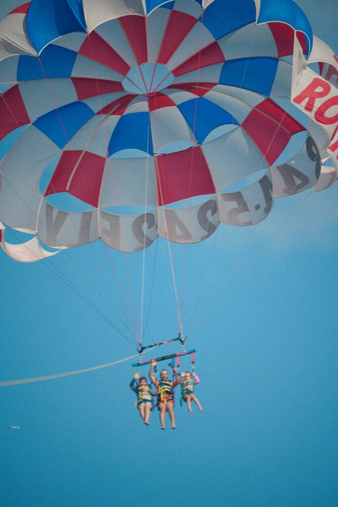 Three riders harnessed beneath the red white and blue Sea Rocket parasail canopy against a clear blue sky