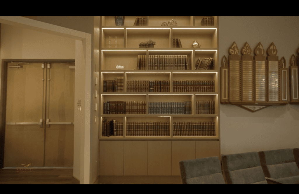 Backlit shelves of Hebrew volumes in the study room, memorial plaques on the wall alongside