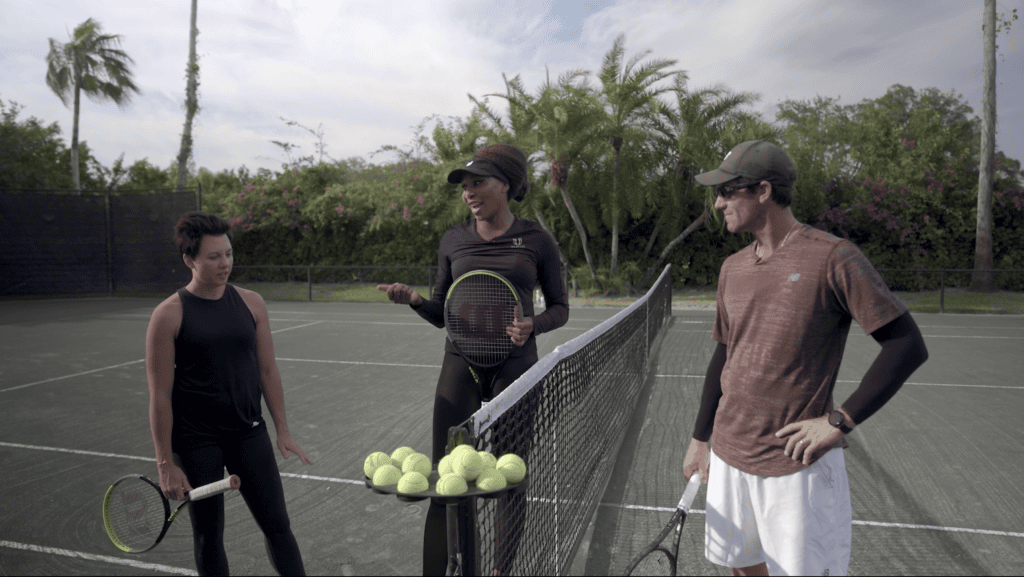 Venus Williams at the net with her coach and a hitting partner, a basket of balls on the court