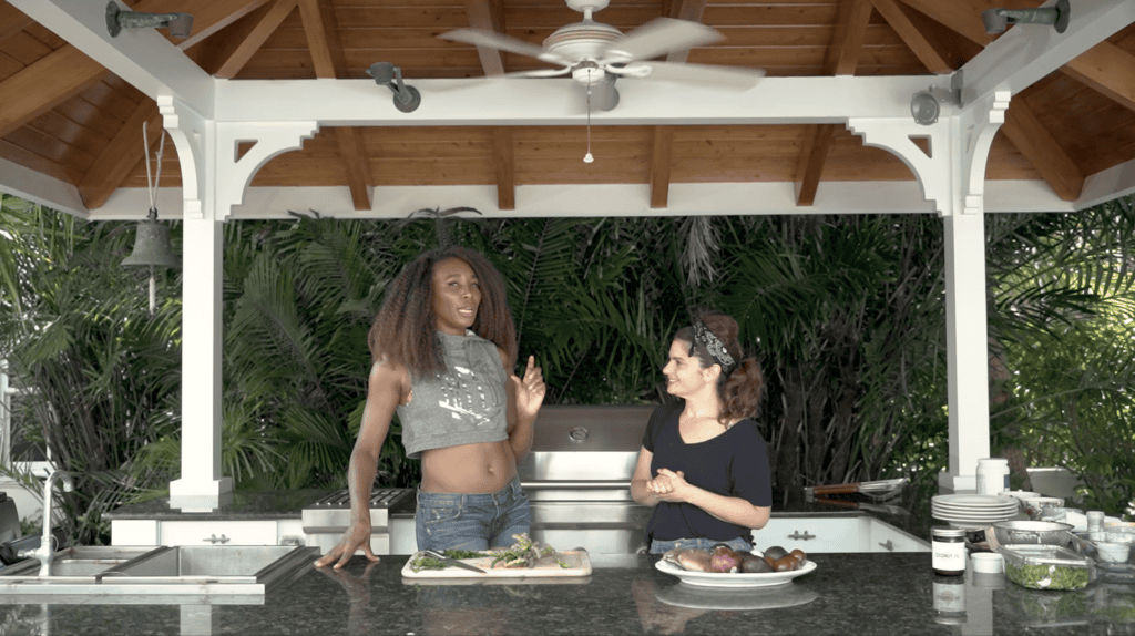 Venus Williams talking with a woman across the counter of a covered outdoor kitchen