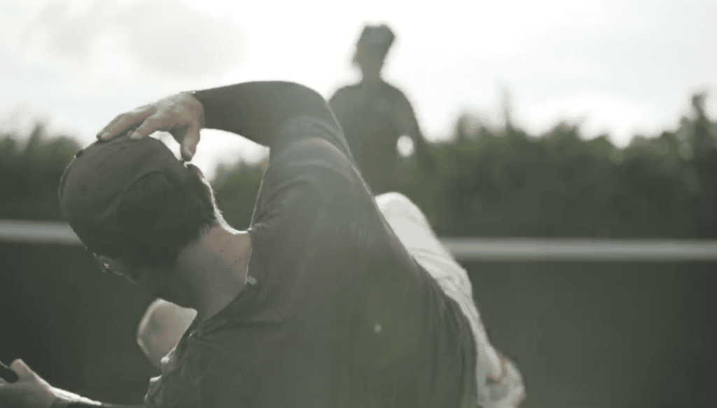 A tennis coach doubled over on the court after taking a ball, a frame from the comedy short