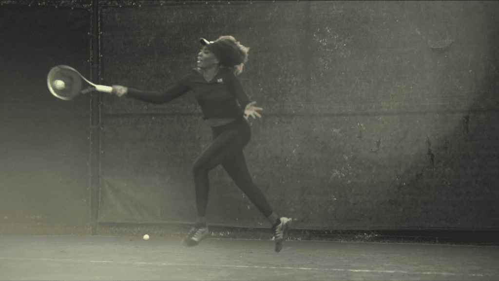 Venus Williams airborne through a forehand on a hazy backlit court, both feet off the ground