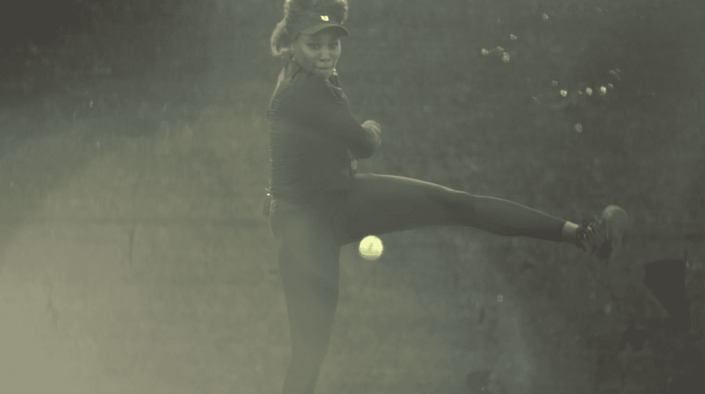 Venus Williams striking the ball on a hazy backlit tennis court, leg extended through the shot