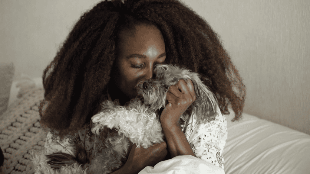 Venus Williams holding her small grey dog close on a bed in soft window light