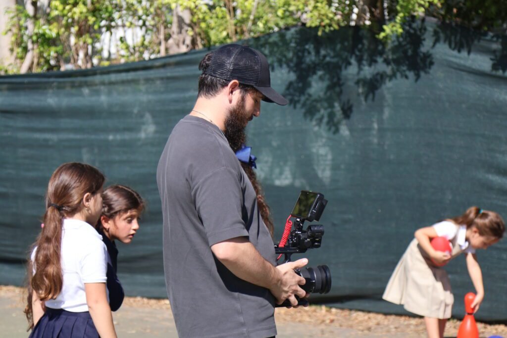 Dov Gurewicz with the gimbal rig on the school court as girls in uniform play around him