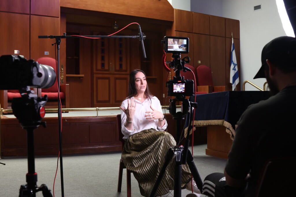 Two-camera interview in the Lanaar School sanctuary, the subject gesturing mid-answer with the boom overhead and an operator at the right
