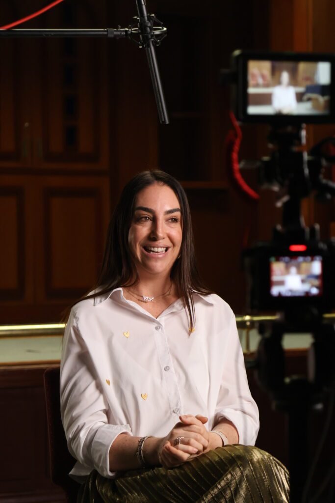 A woman laughing during a filmed interview in the Lanaar School sanctuary, the boom microphone overhead and the camera monitor beside her