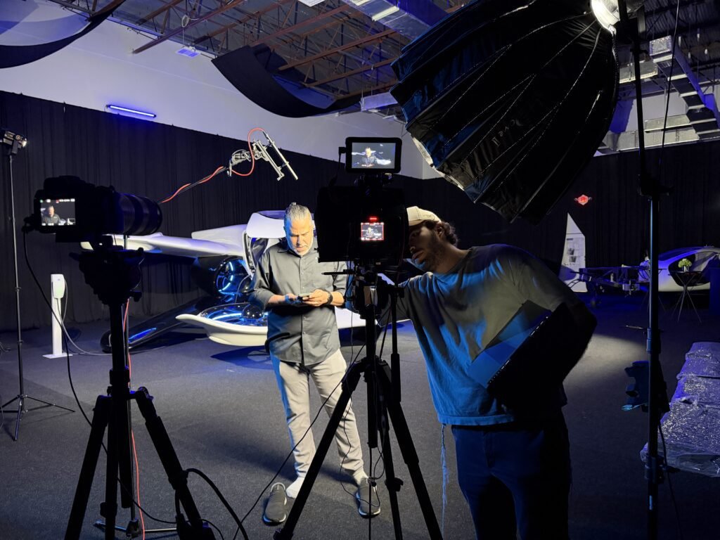 Behind the cameras on the third Doroni shoot, an operator working the rig while a second crew member checks a device, the H1-X lit blue behind them
