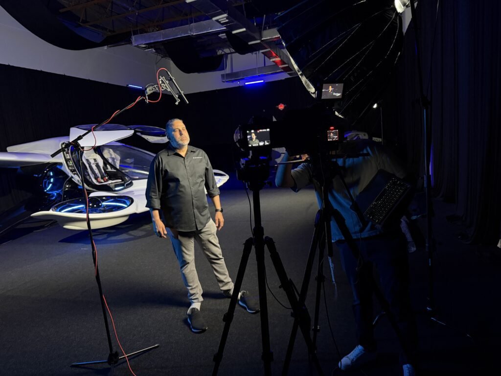 Filming a presenter beside the full-scale H1-X, boom microphone overhead and two cameras with monitors at the right of frame