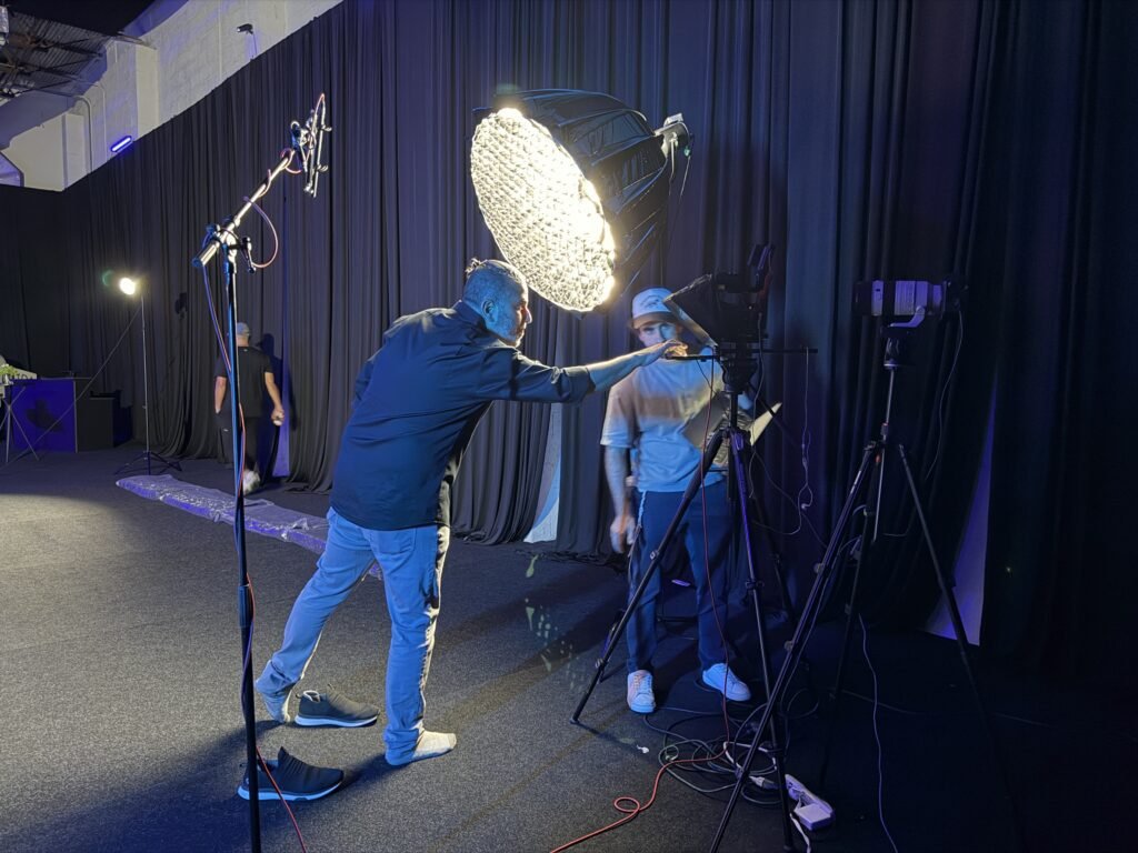 Adjusting the round softbox on the Doroni set, a crew member at the camera behind it and the studio drapes blacked out around them