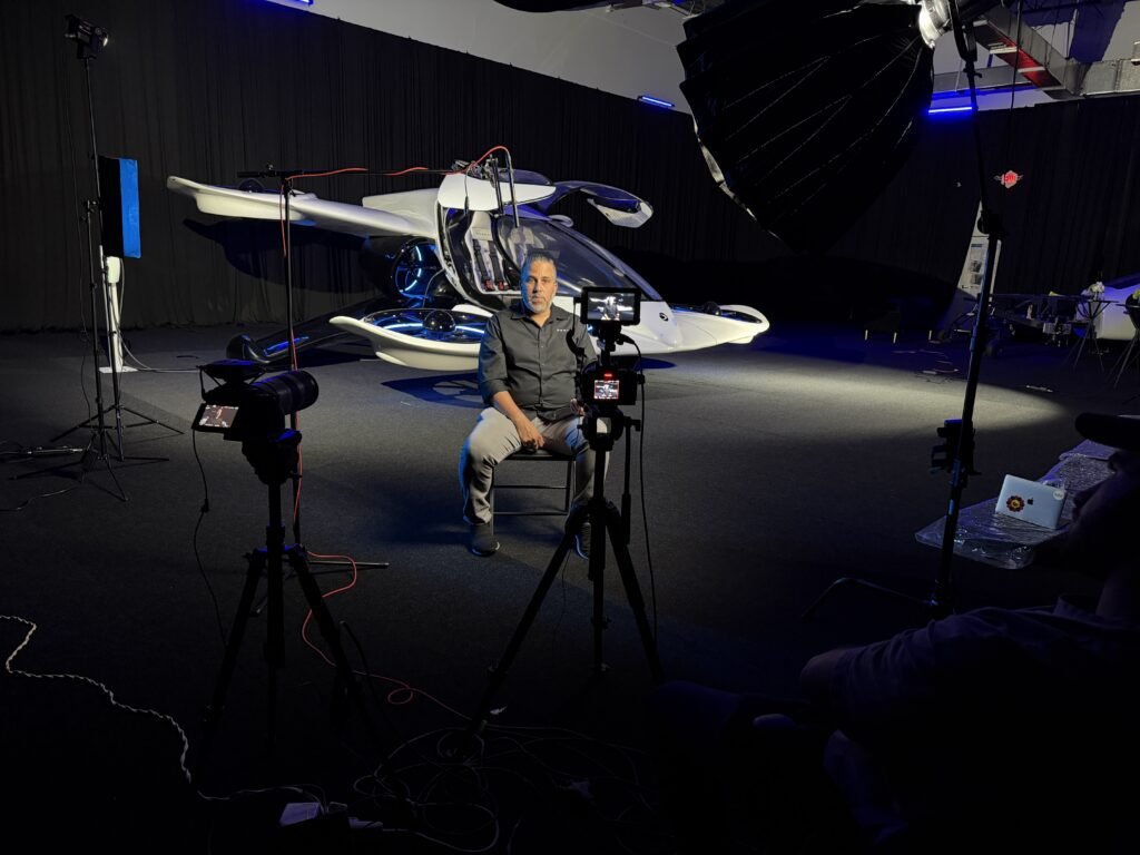 Two-camera interview set in the Doroni studio, the subject seated in front of the full-scale H1-X with its cockpit open and the rotors lit blue