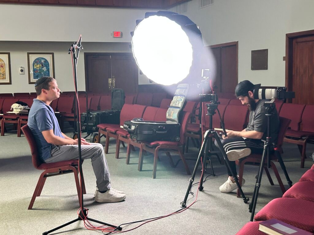 Wide view of a two-camera interview set in the Lanaar School sanctuary, the subject seated at one end and Dov Gurewicz operating from behind a large round softbox