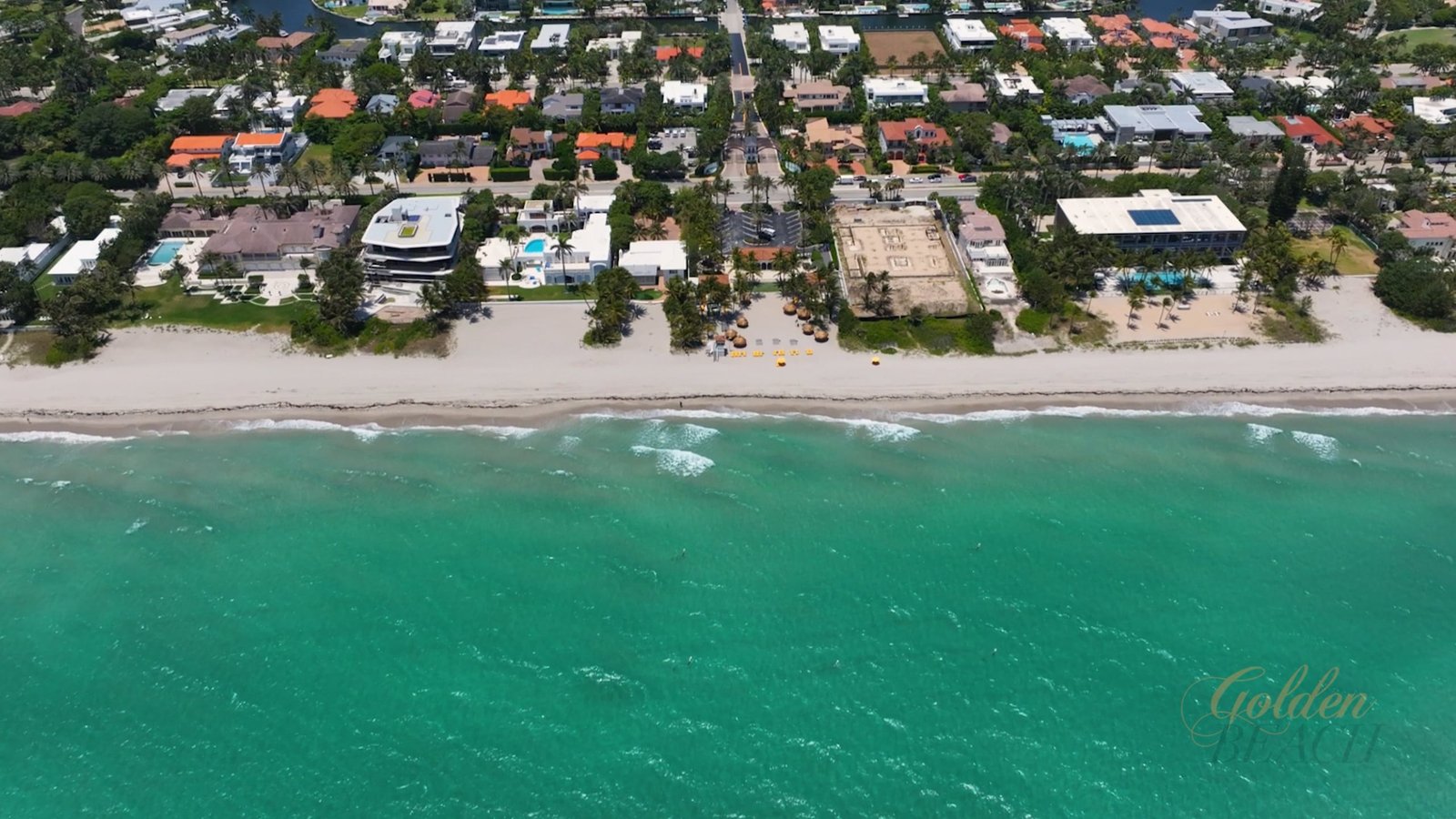 Aerial along the Golden Beach shoreline, oceanfront homes and turquoise water, a frame from the Town of Golden Beach 95th anniversary film